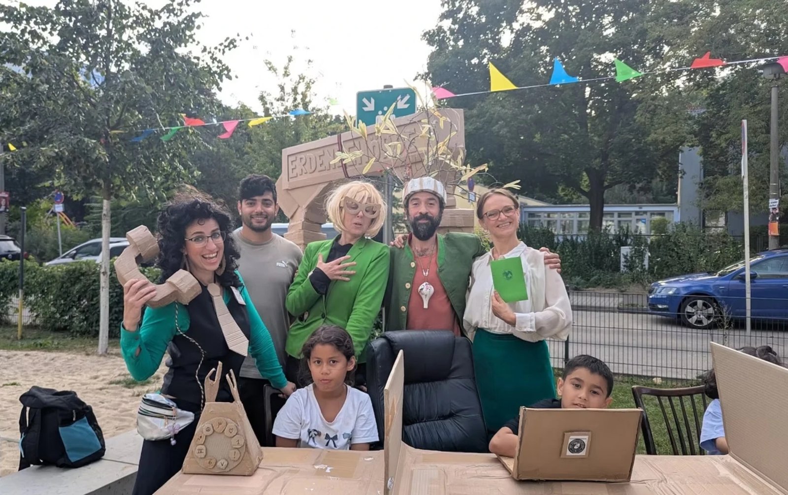 Das kostümierte Team der Erdenbehörde mit Kindern an einem Schreibtisch aus Pappe, darüber bunte Wimpelketten.